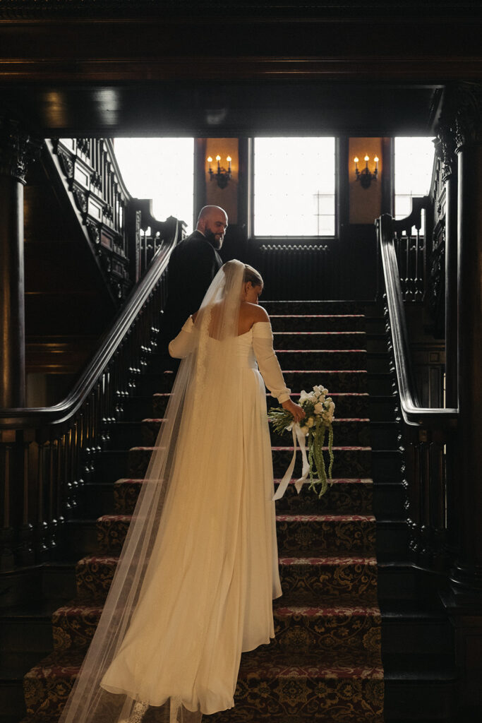Groom helps bride up grand staircase at historic wedding venue Semple Mansion in Twin Cities