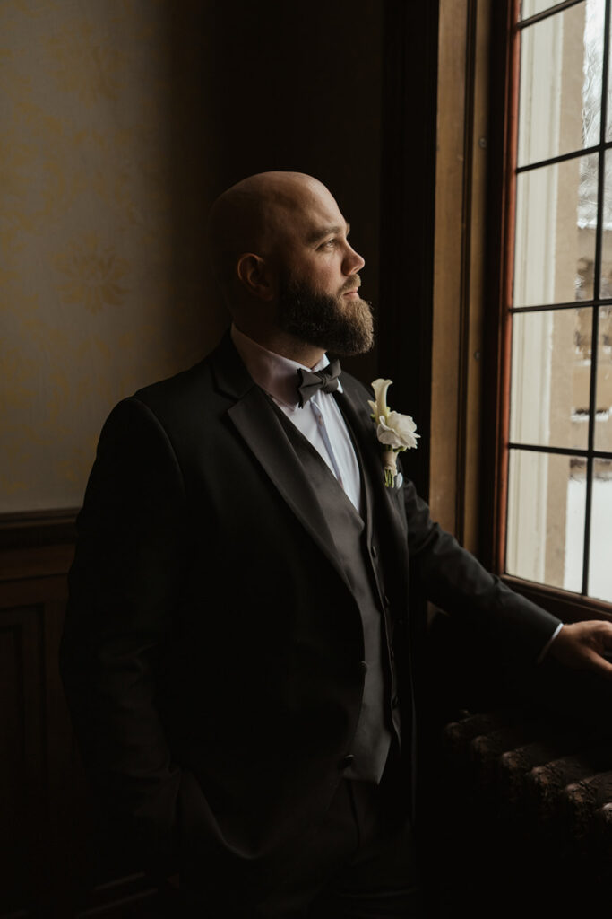 Groom looks out the window at historic wedding venue in Minnesota