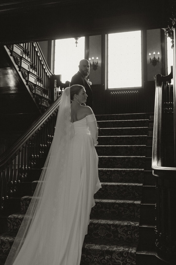 Groom helps bride make her way up grand staircase at Semple Mansion in Twin Cities
