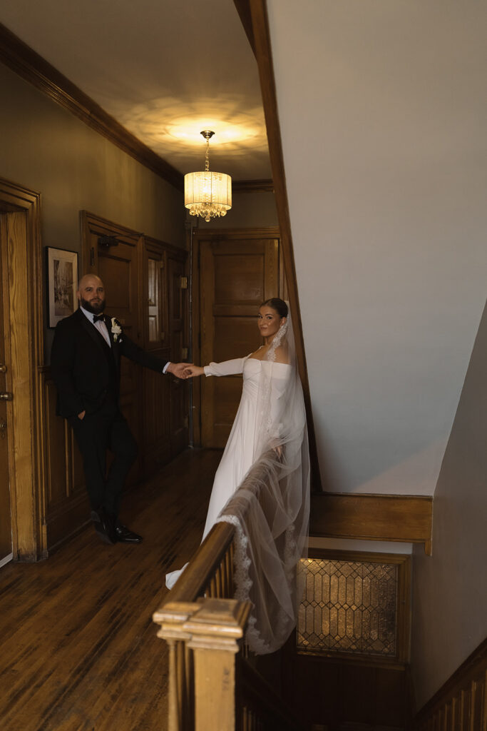 Bride and groom interlace hands while standing on opposite sides of character-filled hallway in Semple Mansion