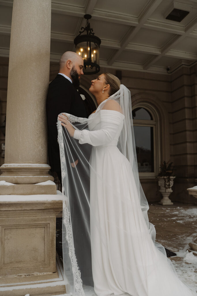 Bride pushes groom gently against a column outside Semple Mansion