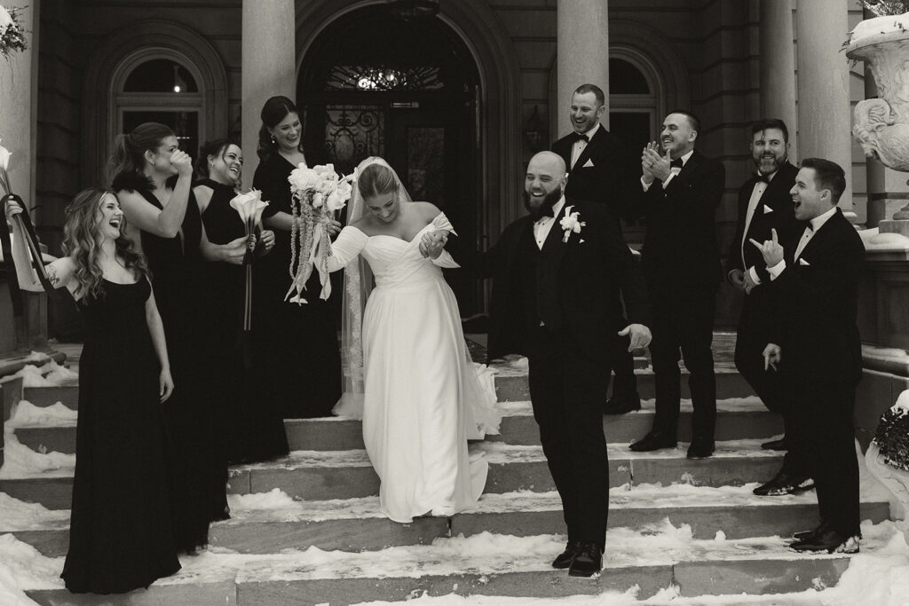 Wedding party cheers as bride and groom walk down the stone steps of mansion wedding venue in Minnesota