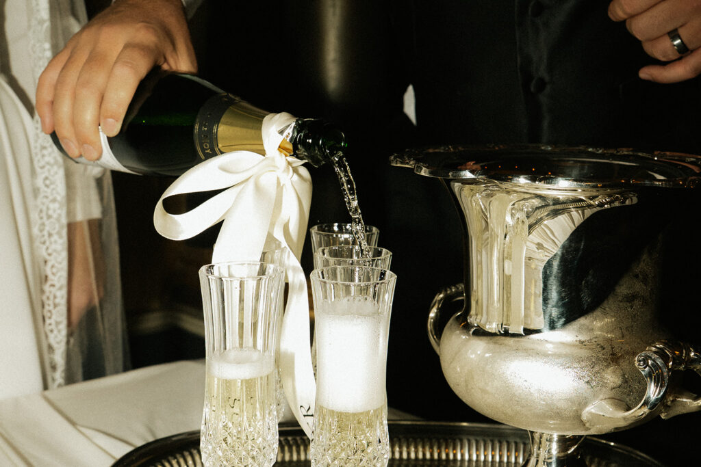 Groom pours champagne with white bow into glasses