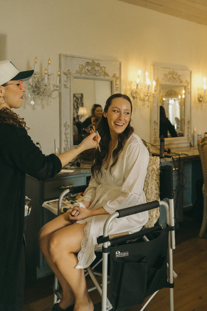 Bride smiles at bridesmaid while she gets her makeup done
