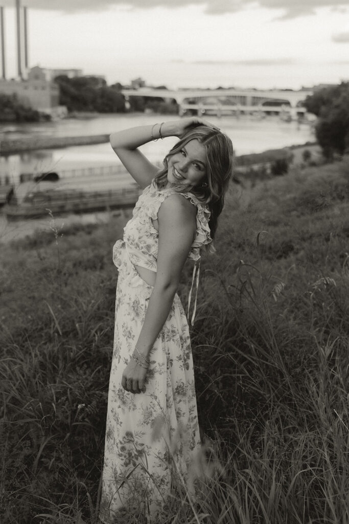 Senior photos of girl standing in tall meadow grass with the city skyline behind her