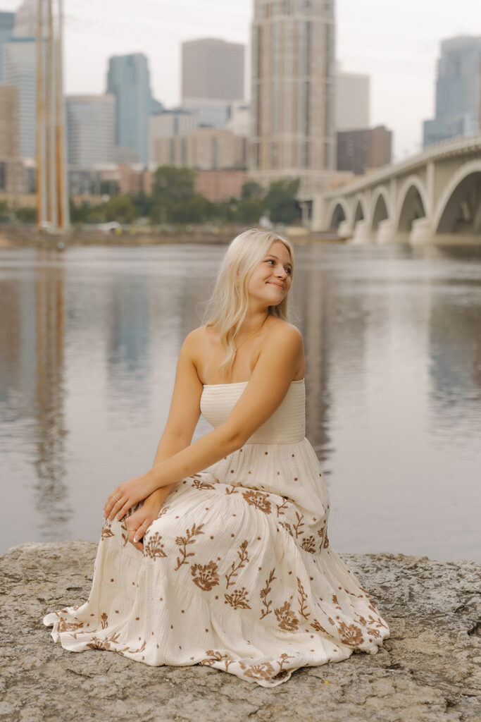Young girl wearing Altar'd State sundress crouches on a rock outcropping in front of the Minneapolis skyline