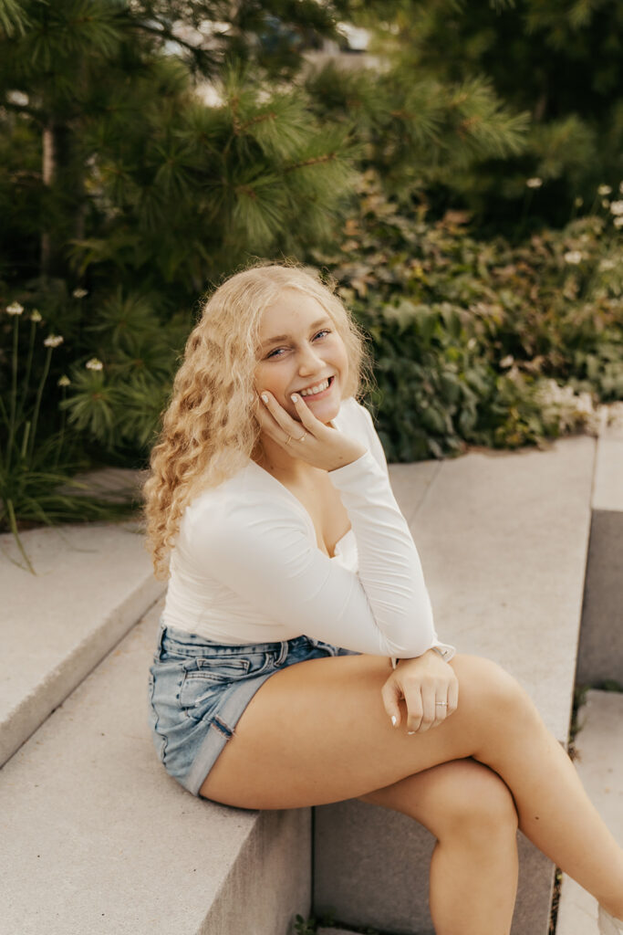 Girl in white long sleeve and denim shorts sits on stone steps with her chin propped in her hand