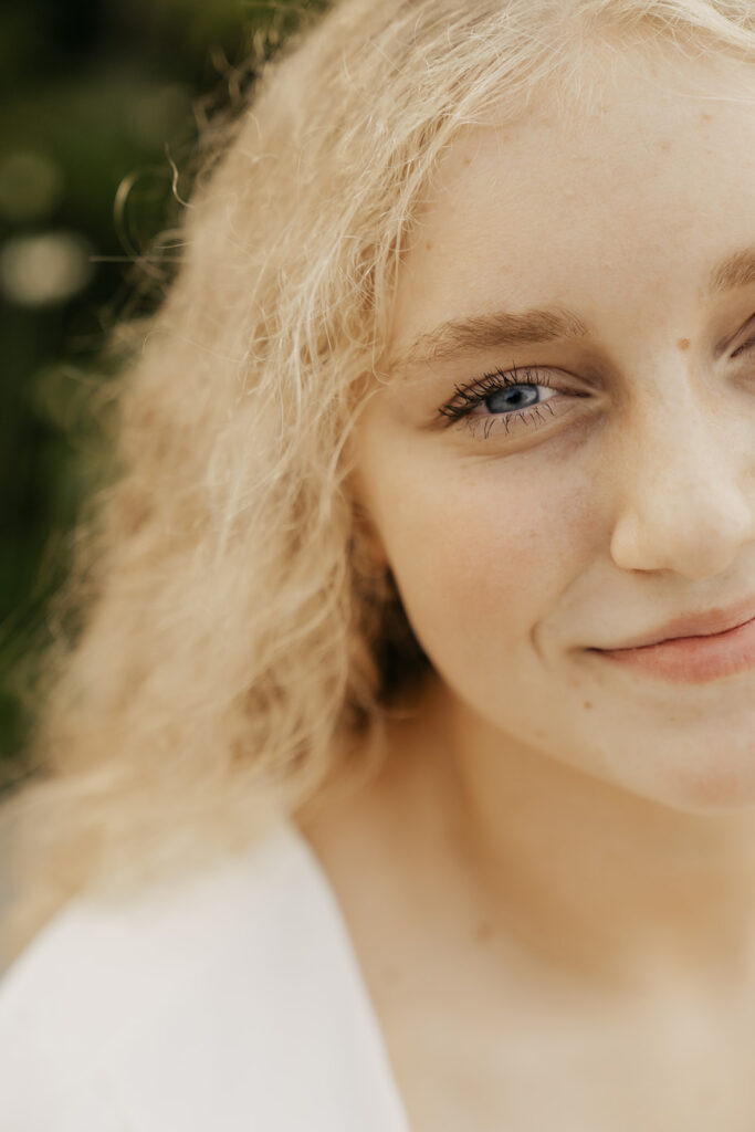 Teenager with blonde hair and blue eyes gives a soft smile to the camera during her senior photos