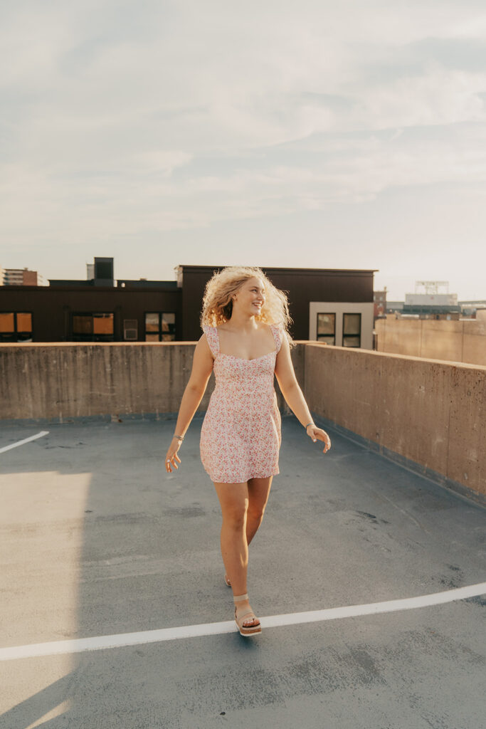 High school senior in pink and white sundress skips across rooftop parking garage in Minneapolis