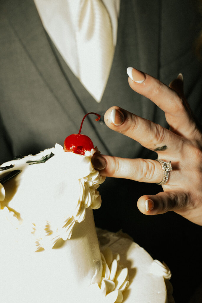Close shot of bride scraping frosting off of a cherry-topped vintage wedding cake