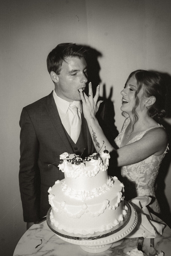Bride feeds groom some frosting off of her ring finger during the cake cutting at wedding