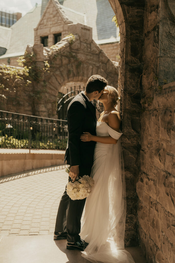 Bride and groom share a kiss in stone archway of mansion wedding venue in Twin Cities